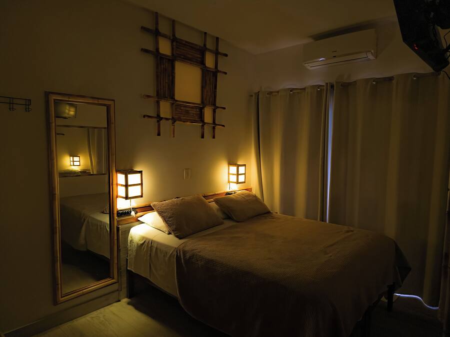A hotel room with a bed, bedside lamps, a mirror, and a ceiling air conditioner.