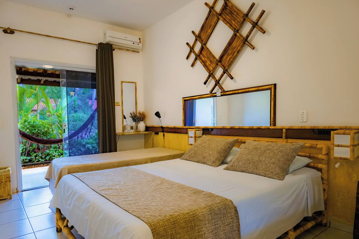 Ett hotellrum med två sängar, en stor spegel, ett litet bord med en lampa och utsikt över grönområden genom en glasdörr.