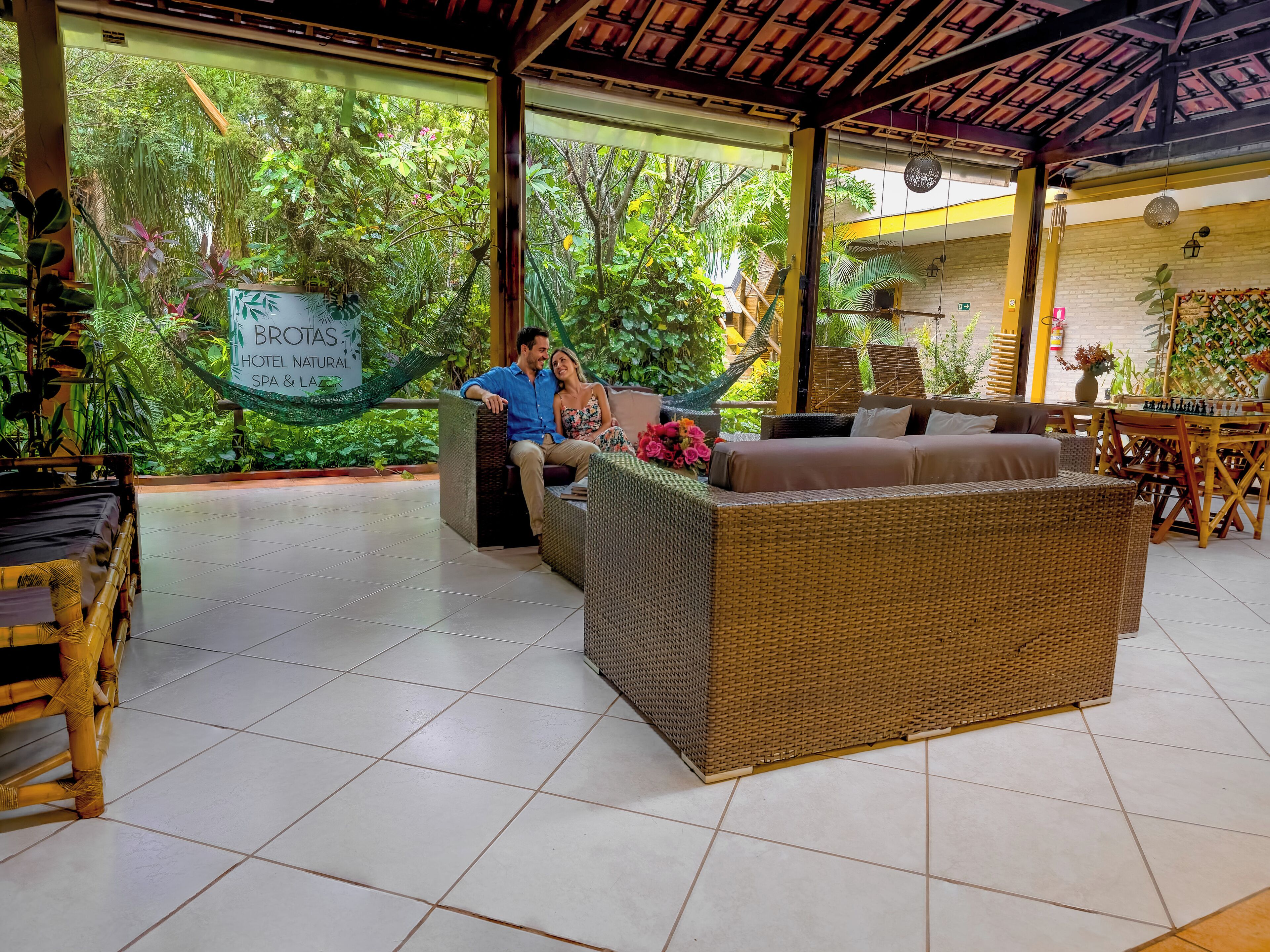 A cozy outdoor seating area with wicker furniture, a hammock, and a sign for 'Brotas Hotel Natural Spa & Laid'.