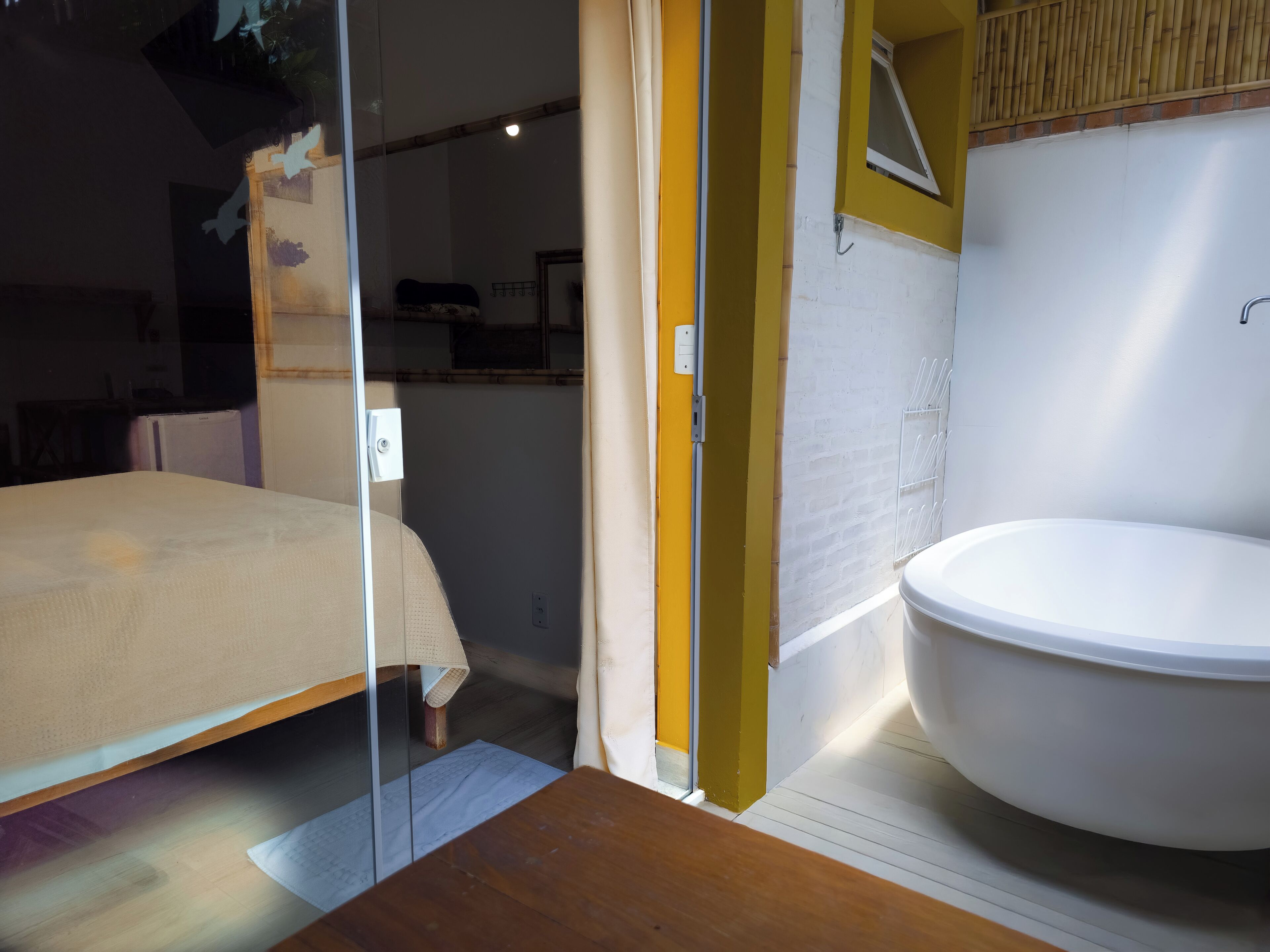 A bedroom with a bed, a wooden floor, a white toilet, and a glass door leading to another room.
