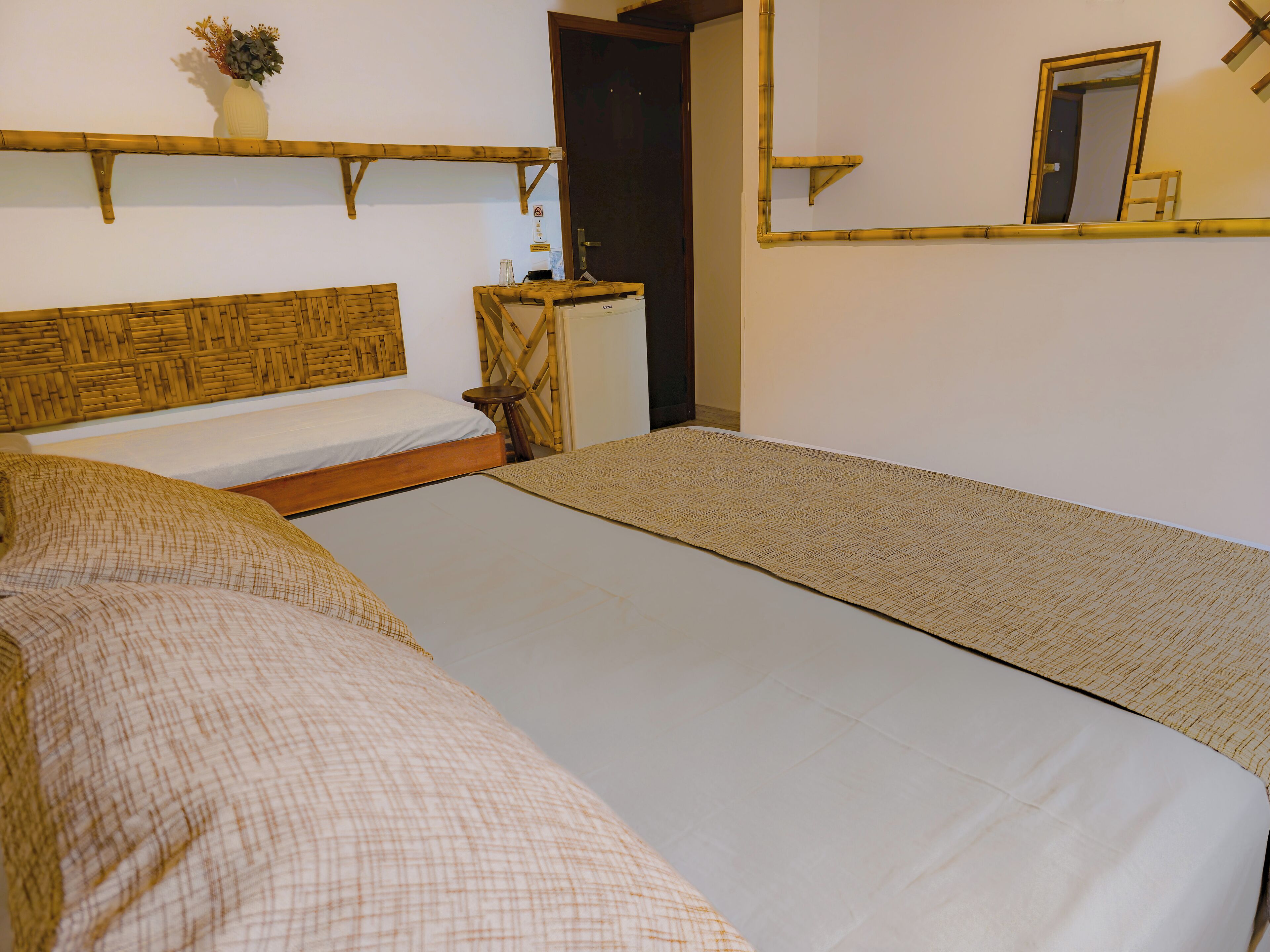 Una habitación con dos camas, una mesita, un espejo y una estantería con un florero.