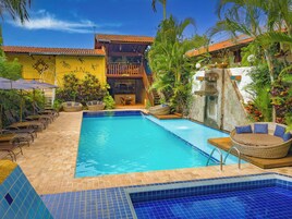 Un área de piscina con suelo de baldosas, sillas de descanso y una zona de bar con vistas a la piscina.