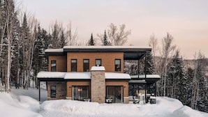 Une maison moderne à deux étages, dotée d’une façade en briques, de grandes fenêtres et d’un espace extérieur couvert.
