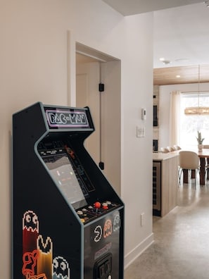 A retro arcade machine in a modern interior with a dining area visible in the background. - Chalet Gratitude | Private SPA & Sauna | Skiing (Saint-Côme)