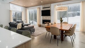 Un salon moderne doté d’une cheminée, d’un coin repas et de grandes fenêtres.