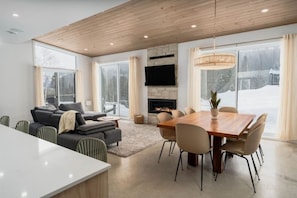 Un salon moderne doté d’une cheminée, d’un coin repas et de grandes fenêtres.