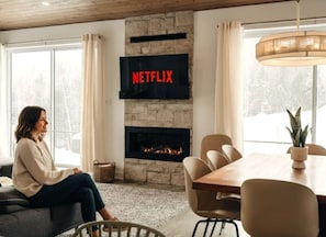 A cozy living room with a fireplace, a television mounted on the wall, and a dining area. - Chalet Gratitude | Private SPA & Sauna | Skiing (Saint-Côme)