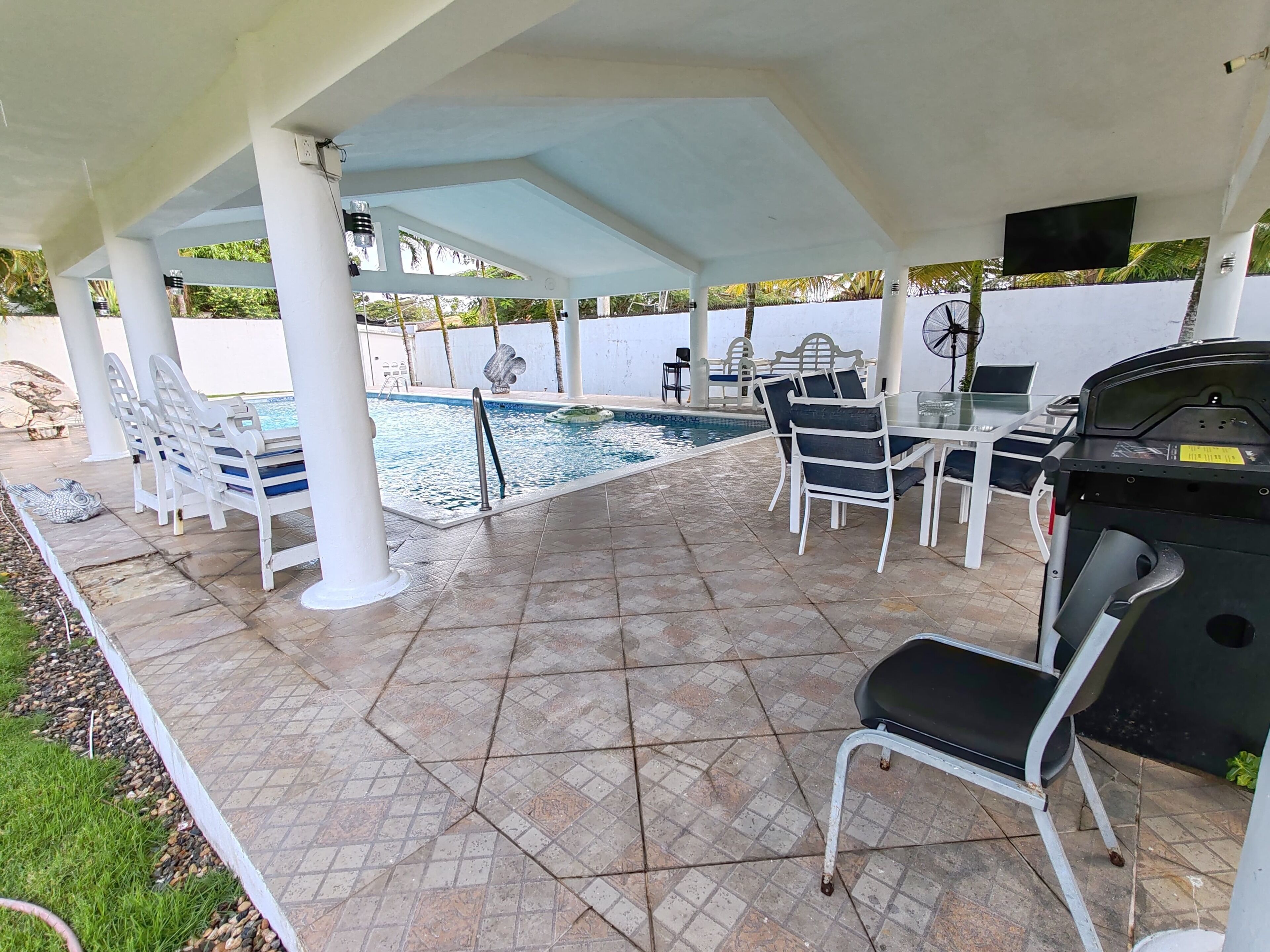 An outdoor pool area with a covered patio, seating, and a grill.