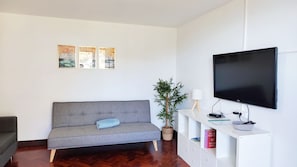 A living room with a grey sofa, a flat-screen TV, a potted plant, and a wall-mounted shelf with a remote control. - Villa Rodrigues 2 by Rentallido (Campanario)