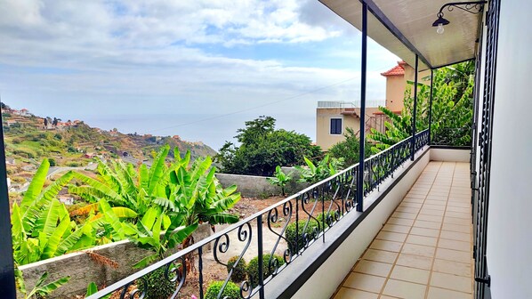A balcony with a view of a hillside, a tiled floor, and a metal railing.