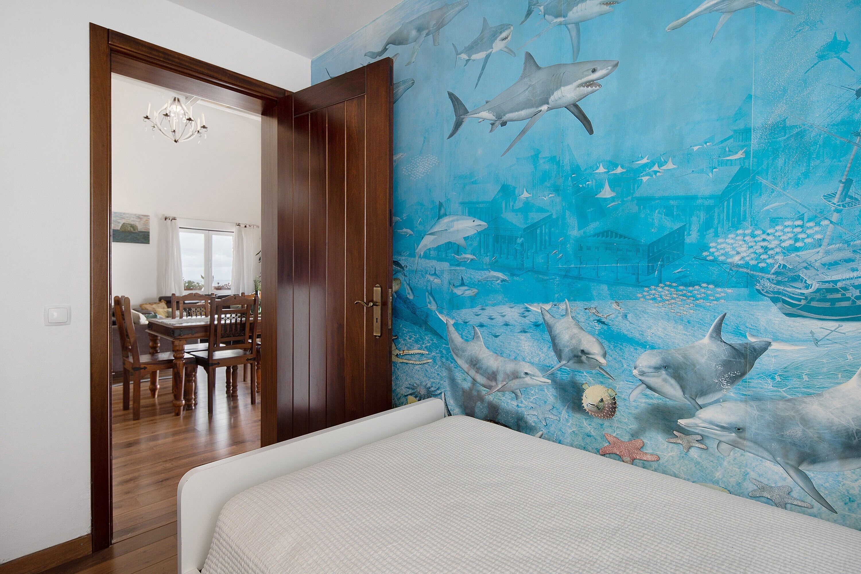 Une chambre avec une fresque représentant la vie marine, une porte en bois et une vue sur un coin repas.