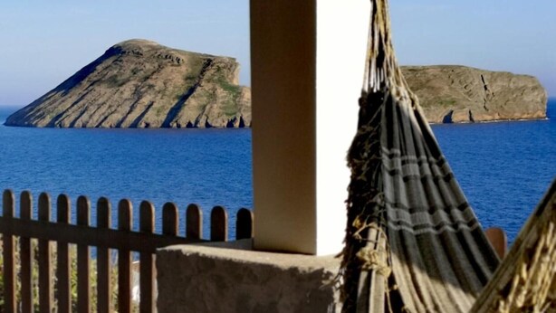 Eine Hängematte auf einer gefliesten Terrasse mit Blick auf das Meer und eine felsige Insel.