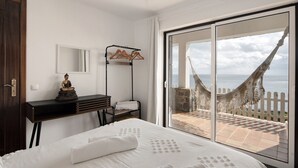 Ein Hotelzimmer mit Bett, Schreibtisch, Stuhl, einem großen Fenster mit Meerblick und einer Hängematte außen.