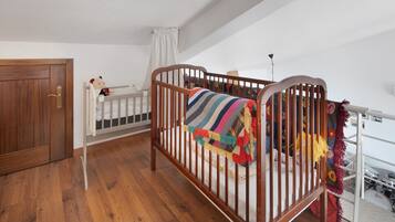 Una culla in legno con una coperta a righe colorate, una culla bianca con un orsacchiotto e una porta in legno.