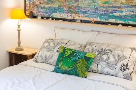 A bed with white bedding, a green and black patterned pillow, a yellow lamp, and a wall with a colorful abstract painting.. Charming Apartment in Village Center