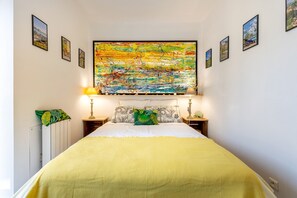 Une chambre à coucher avec un lit, une grande peinture abstraite au-dessus du lit et des tableaux encadrés accrochés aux murs.