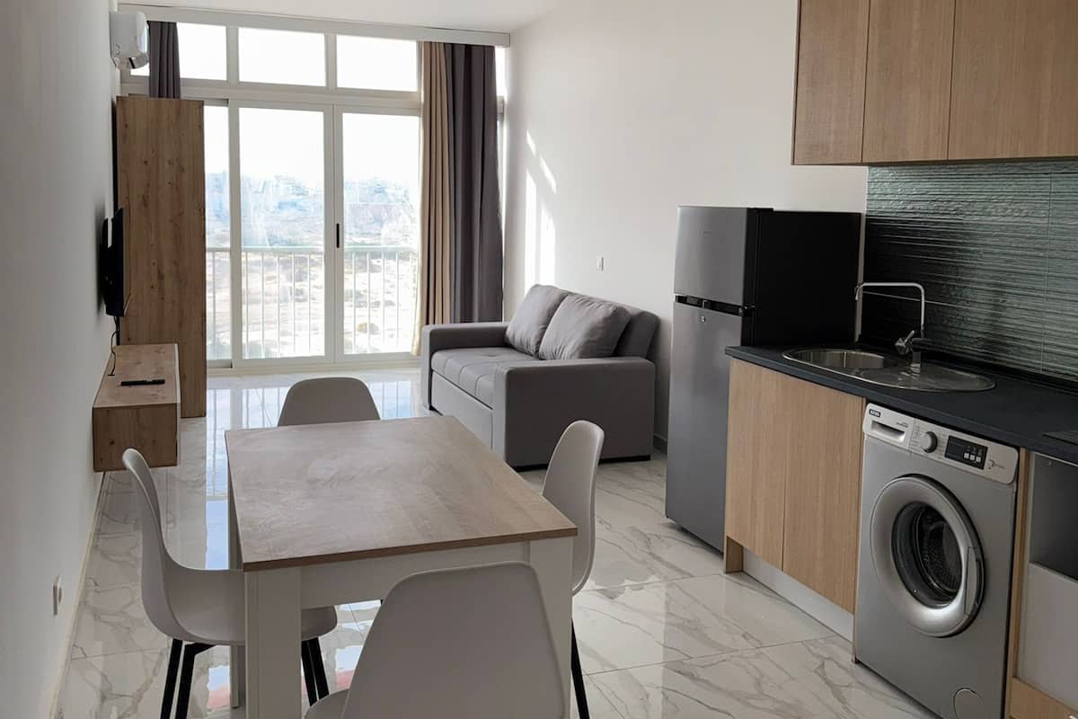 A modern apartment with a dining area, sofa, kitchen, and large windows.