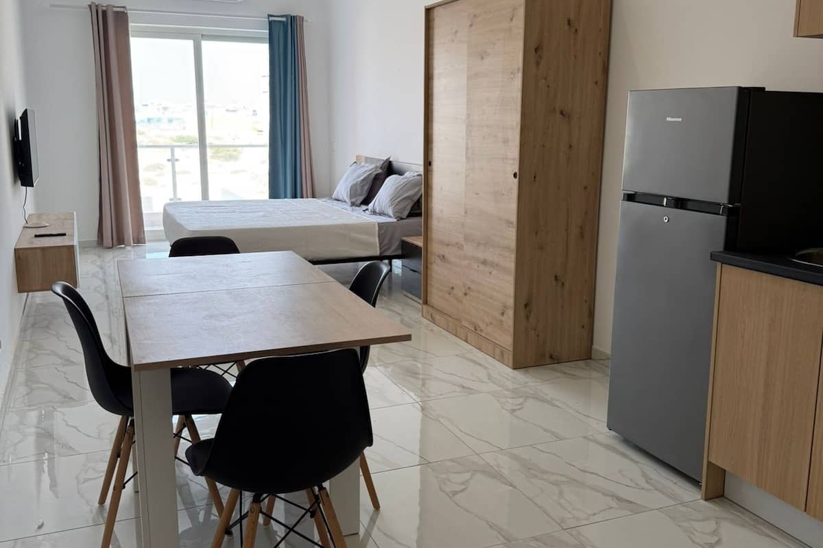 A modern kitchen with a dining area, a wooden wardrobe, and a large window.