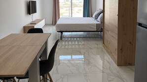 Une chambre d’hôtel moderne, dotée d’un bureau en bois, d’un lit, d’une armoire et offrant une vue sur l’extérieur.