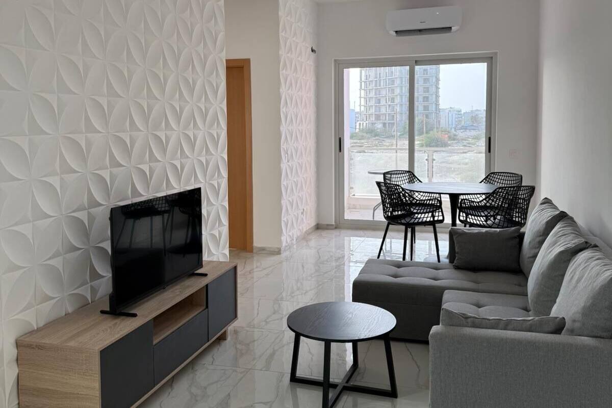 A modern living room with a TV on a wooden stand, a grey sofa, a round coffee table, and a patterned wall.