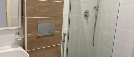 Un baño con ducha de mampara de vidrio, inodoro blanco y lavabo con espejo.