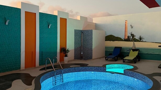 Un espace piscine intérieur moderne, avec une piscine aux carreaux bleus, des chaises longues et une fresque au plafond.