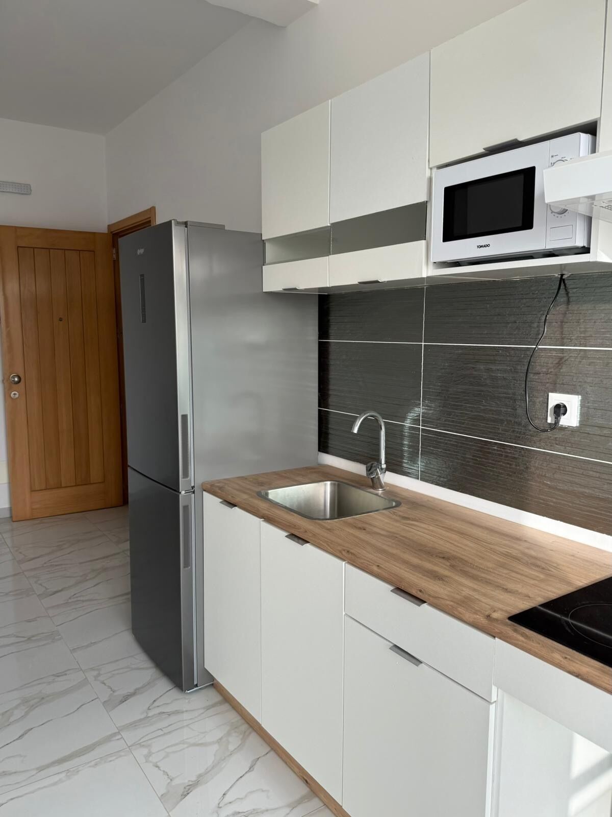Une cuisine moderne équipée d’un réfrigérateur en acier inoxydable, d’un four à micro-ondes et d’un évier avec un plan de travail en bois.