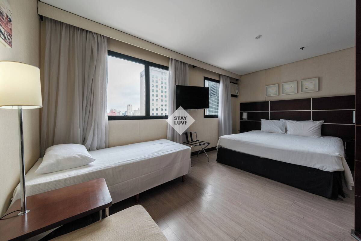 Ein Hotelzimmer mit zwei Betten, einem Schreibtisch, einem Stuhl, einem Fernseher und einem 'STAY LUV' Schild.