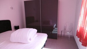 Een slaapkamer met een bed, een kledingkast, een stoel en een nachtkastje.