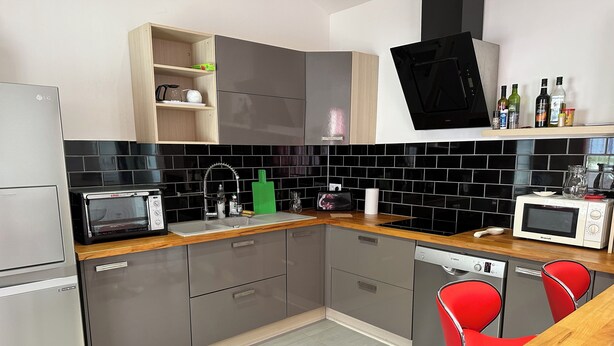 Een moderne keuken met grijze kastjes, een houten aanrechtblad, een Bosch vaatwasser, een rode stoel en een zwart betegelde spatwand.