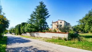 A residential street with a two-story house, a stone wall, and a large tree. - Cozy Apartment With Shared Pool (Umag)