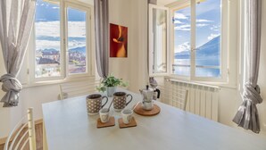 A dining area with a table set for four, a coffee maker, and a view of a mountainous landscape through large windows. - Breathtaking Lake View (Varenna)