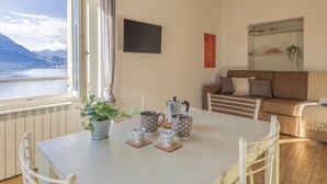 A dining area with a table set for two, a potted plant, and a view of a lake with mountains in the background. - Breathtaking Lake View (Varenna)