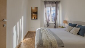 A bedroom with a large bed, a window with curtains, a bedside table with a lamp, and a wall-mounted picture. - Breathtaking Lake View (Varenna)