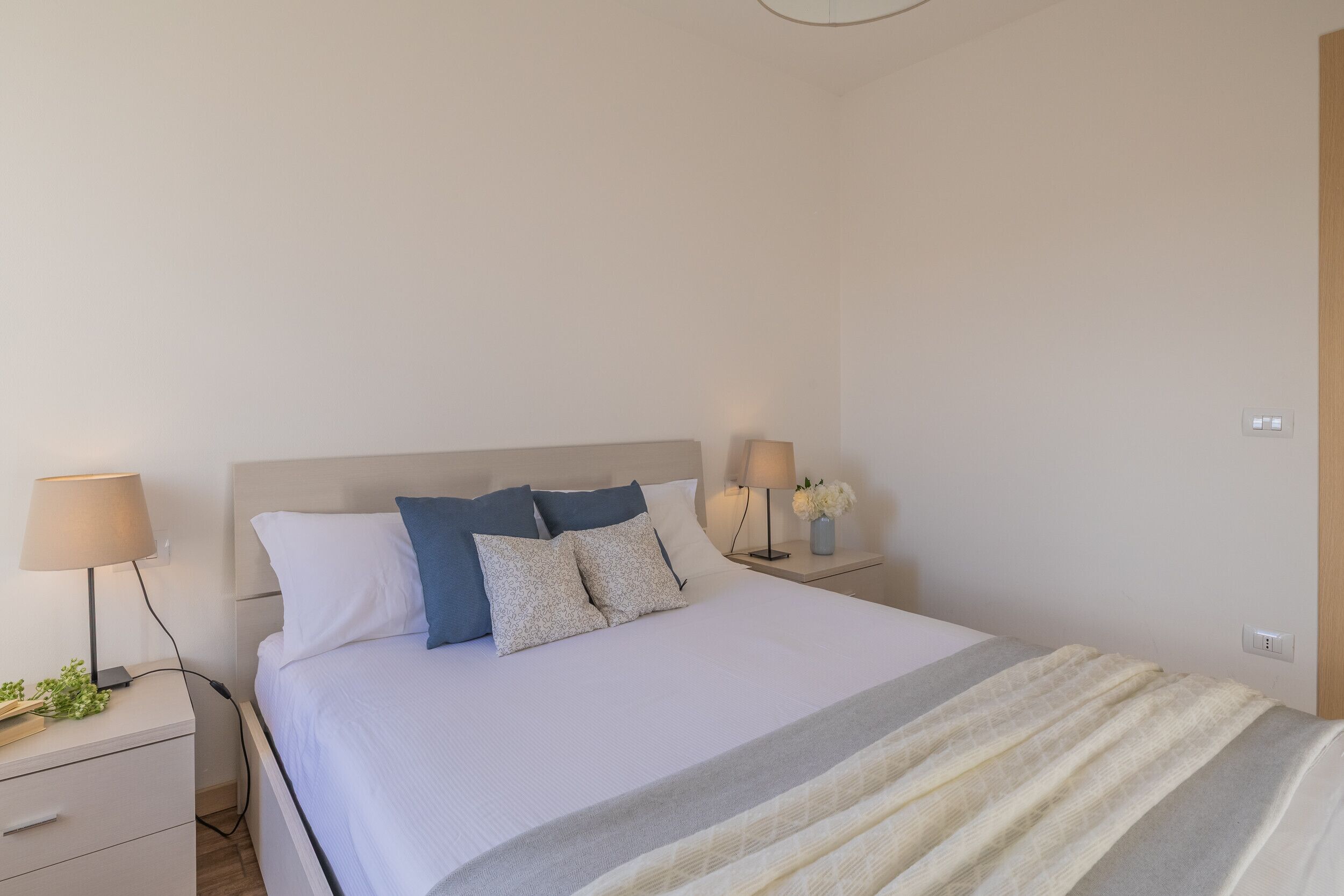 A neatly arranged bedroom with a bed, bedside tables, lamps, and a nightstand.