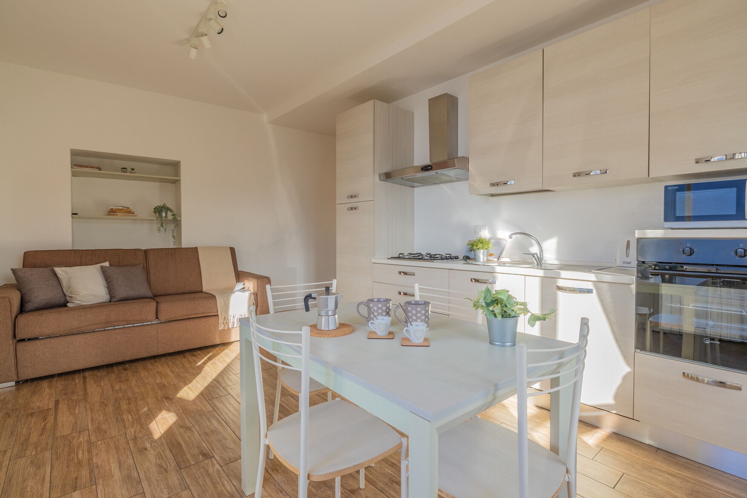 A modern kitchen with white cabinets, a dining table with chairs, and a sofa in the living area.