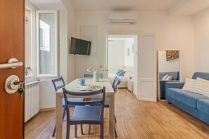 A compact living space with a dining area, a sofa, a TV mounted on the wall, and a door with a handle. - Dream Lake Home in Varenna (Varenna)