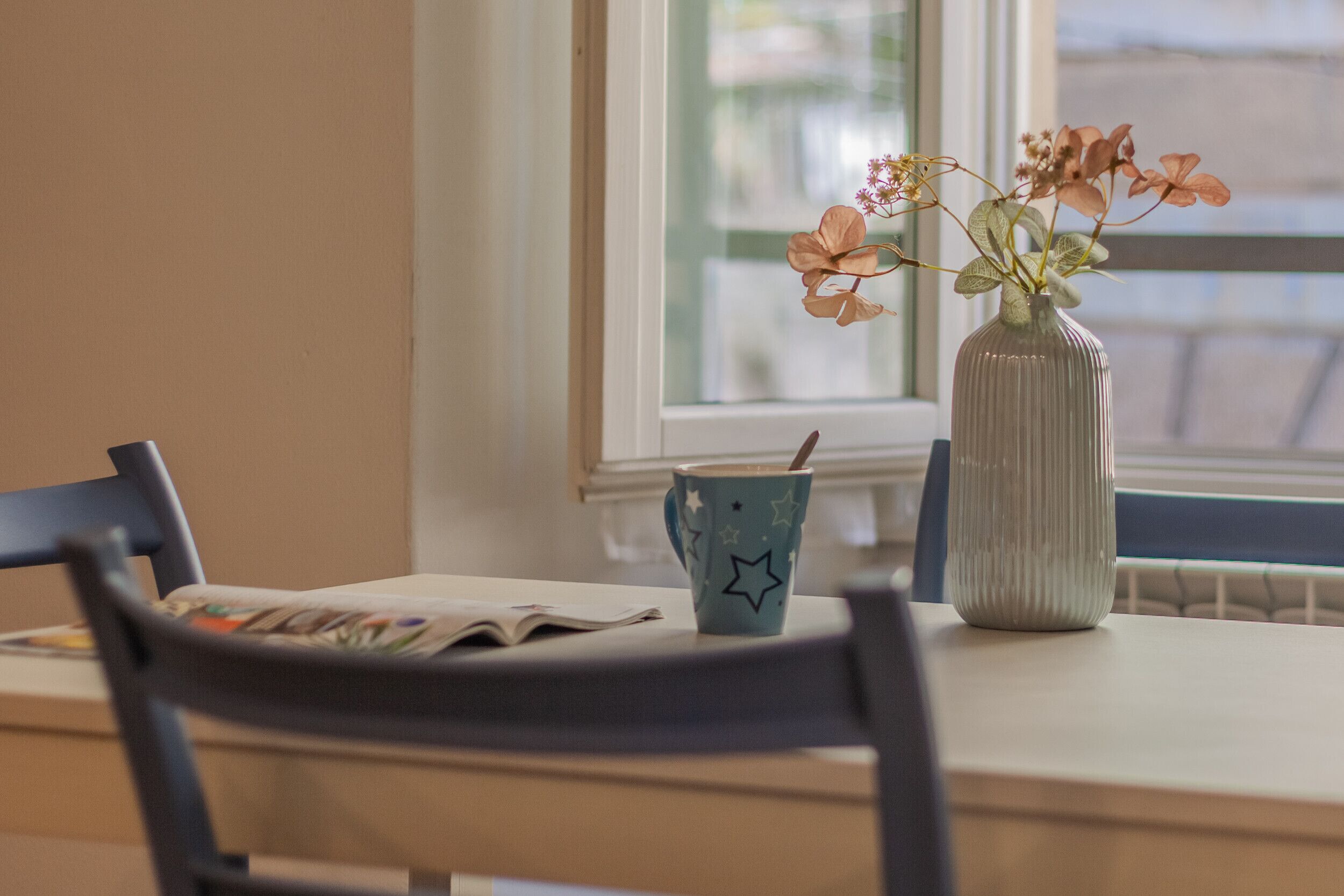 A dining table with a vase of flowers, a star-patterned mug, and a chair.