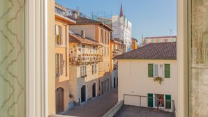 A narrow street with buildings on either side, featuring balconies with plants, a clear sky, and a church spire in the background. - Dream Lake Home in Varenna (Varenna)