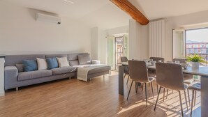 Ein modernes Wohnzimmer mit grauem Sofa, Holzboden und einem Essbereich mit Stühlen und Tisch.