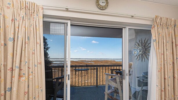 Un balcón con vista a la playa, una mesa de madera y sillas.