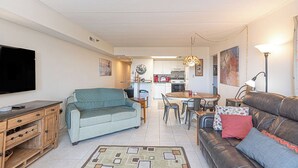 Una sala de estar con sofá, televisión, mesa de comedor con sillas y cocina al fondo.