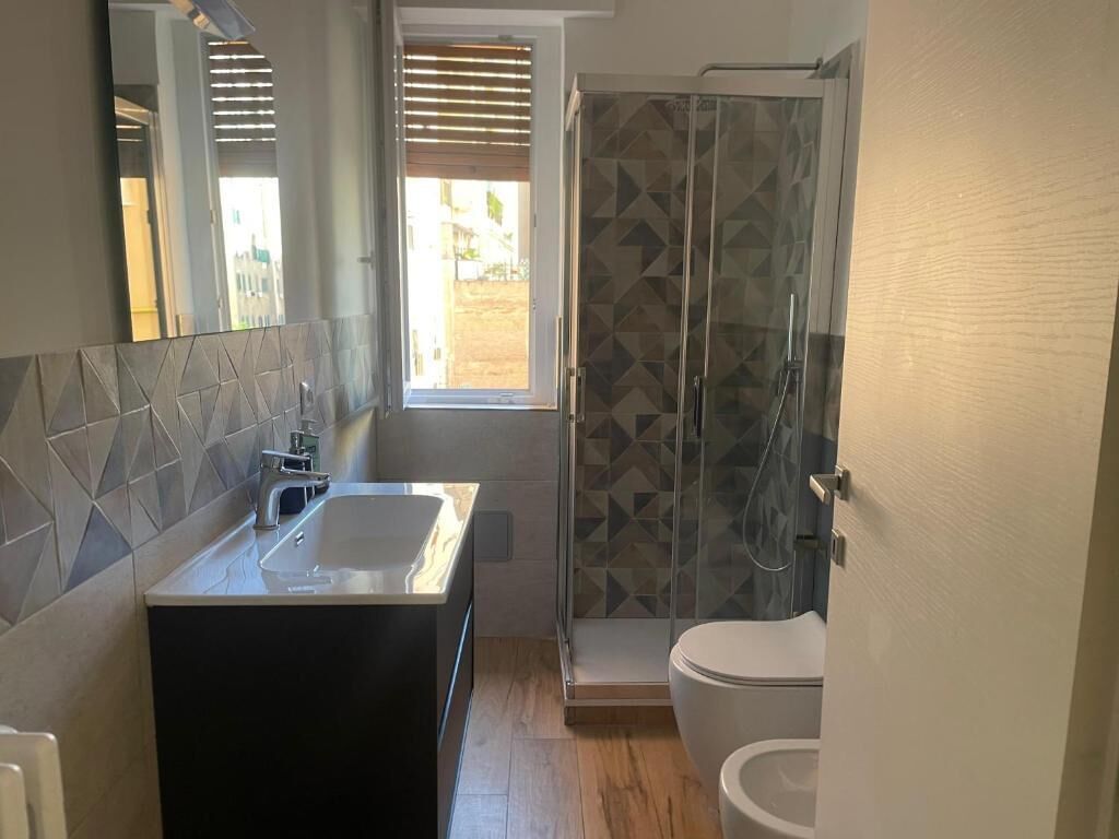 A bathroom with a modern design, featuring a large sink, a toilet, and a shower area with a geometric tile pattern.