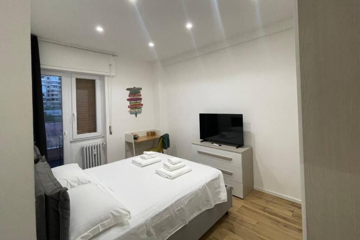 A modern bedroom with a bed, a TV, a small bedside table, and a window.