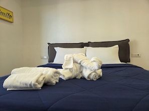 A bed with a dark blue quilt, white pillows, and a rolled-up white towel.