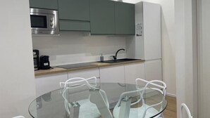 A modern kitchen with a microwave, sink, and green cabinets. There is a glass table with white chairs. - Imperatore suites (Rome)