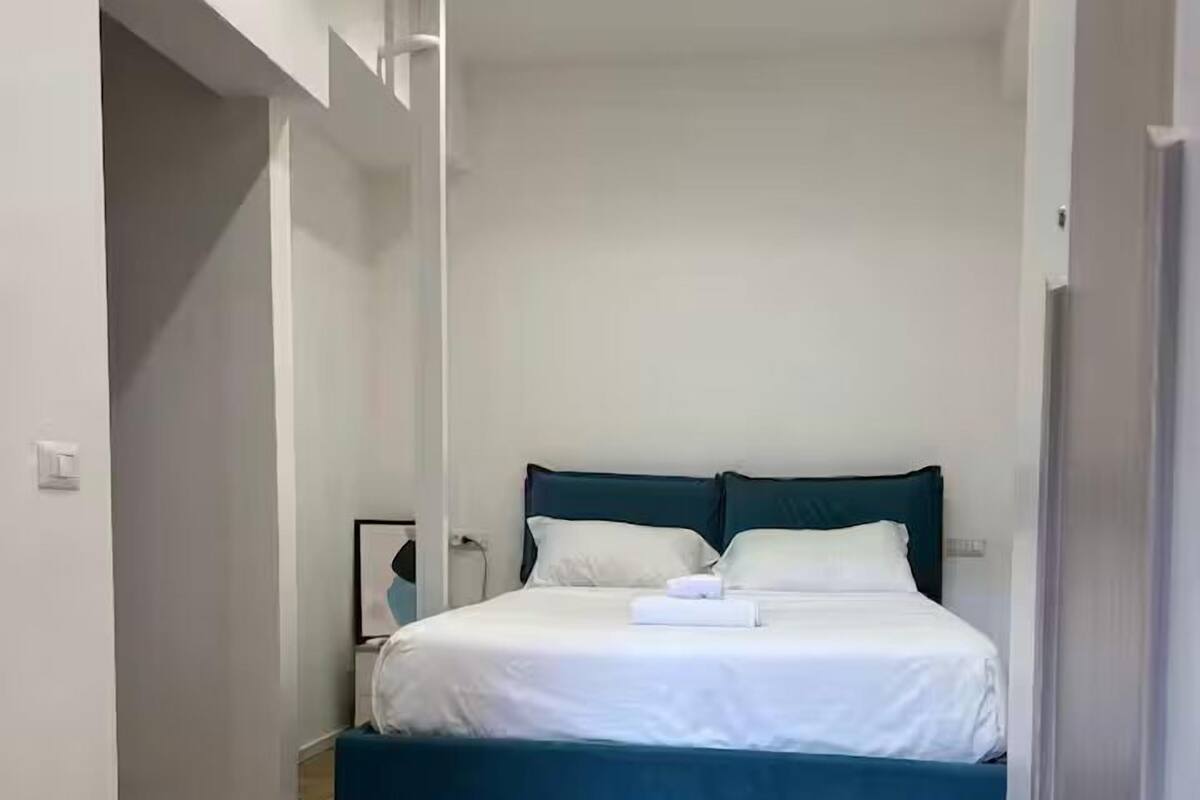 A bedroom with a bed, wooden flooring, and a white wall.