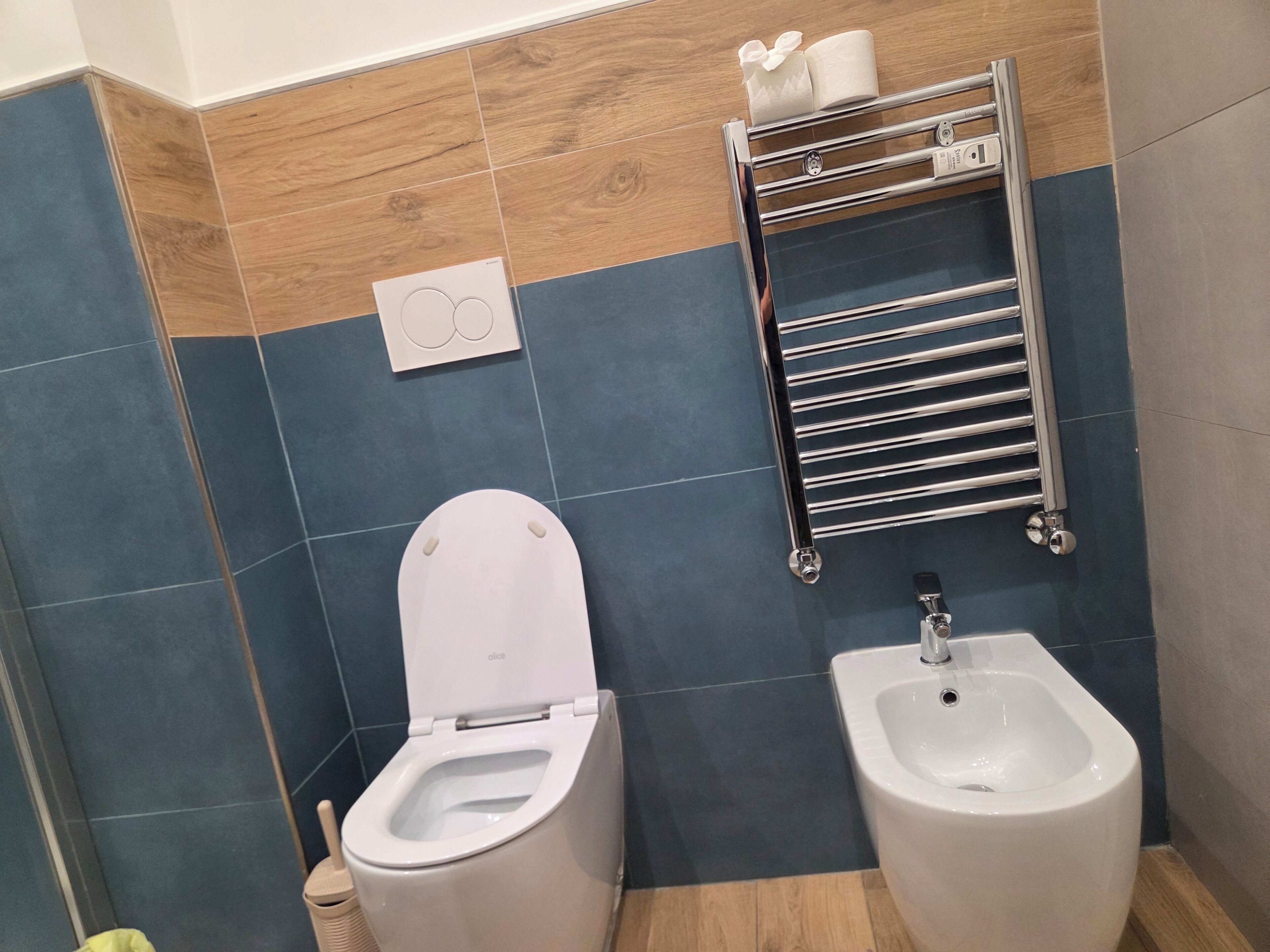 A bathroom with a toilet, bidet, and a towel rack with two rolls of toilet paper.