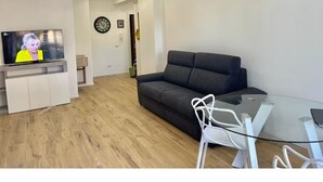 A modern living room with a flat-screen TV, a dark sofa, a glass coffee table, and a white chair. - Imperatore suites (Rome)