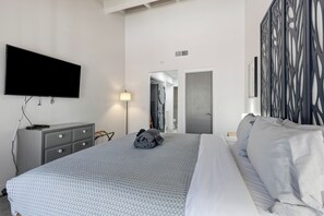 Ein modernes Hotelzimmer mit einem großen Bett, einem flachbildfernseher an der Wand, einer grauen Kommode und einer dekorativen Wandverkleidung.